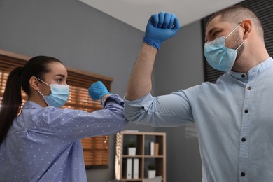 Photo of Office employees in masks greeting each other by bumping elbows at workplace