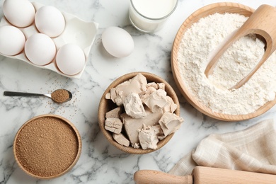 Photo of Yeast and ingredients for dough on white marble table, flat lay