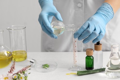 Scientist developing cosmetic oil at white wooden table, closeup