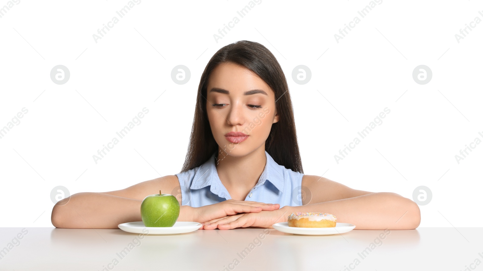 Photo of Woman choosing between apple and doughnut at table on white background