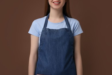 Photo of Woman wearing kitchen apron on brown background, closeup. Mockup for design