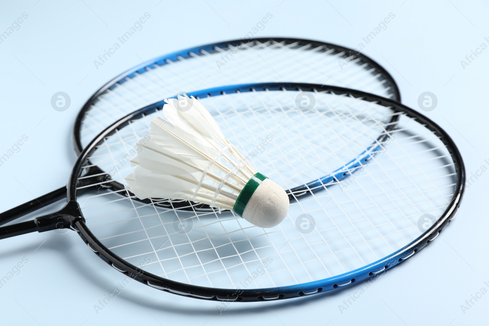 Photo of Feather badminton shuttlecock and rackets on light blue background, closeup