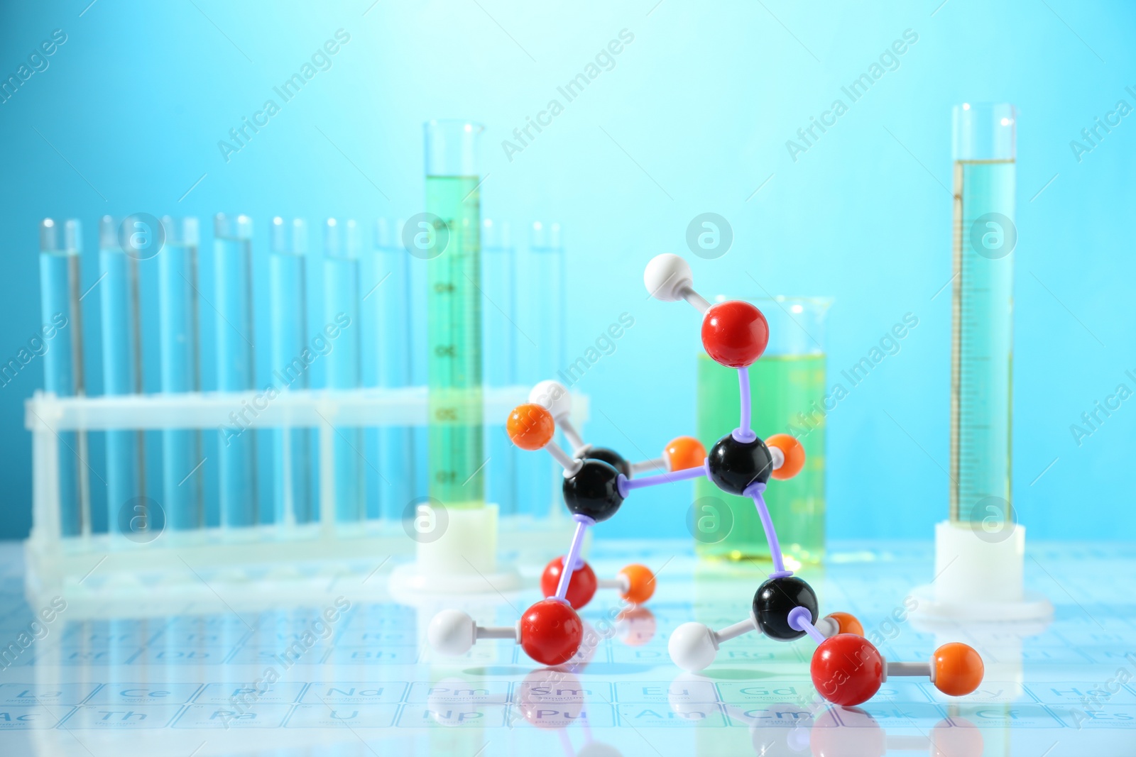 Photo of Molecular model and laboratory glassware on mirror surface against light blue background