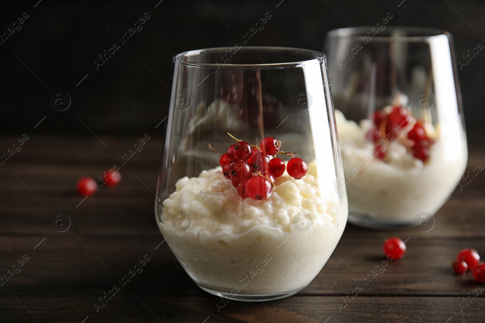 Photo of Creamy rice pudding with red currant in glass and berries on wooden table