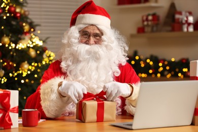 Photo of Santa Claus decorating Christmas gift with ribbon at home