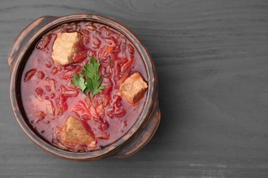 Photo of Tasty borscht in bowl on grey wooden table, top view. Space for text