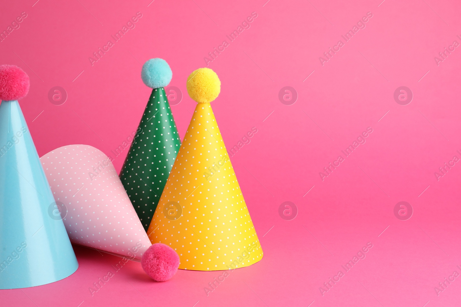 Photo of Beautiful party hats with pompoms on pink background, space for text