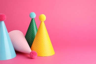 Beautiful party hats with pompoms on pink background, space for text
