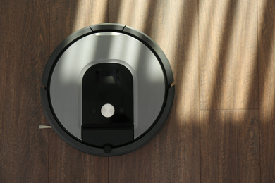 Modern robotic vacuum cleaner on wooden floor, top view. Space for text