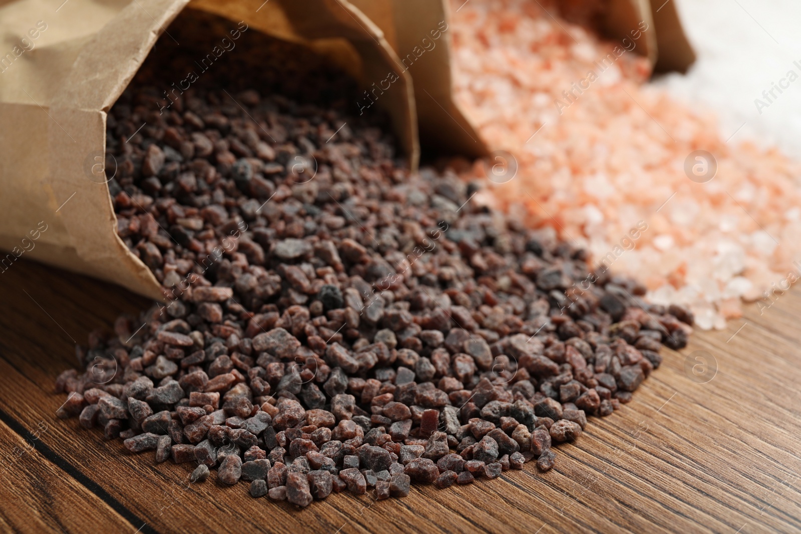 Photo of Paper bags with different kinds of salt on wooden table, closeup