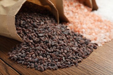 Paper bags with different kinds of salt on wooden table, closeup