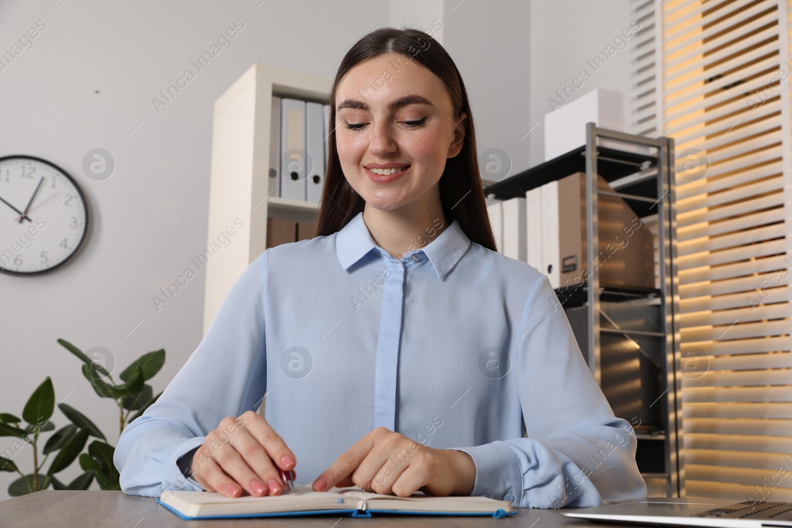 Photo of Happy woman taking notes at wooden table in office