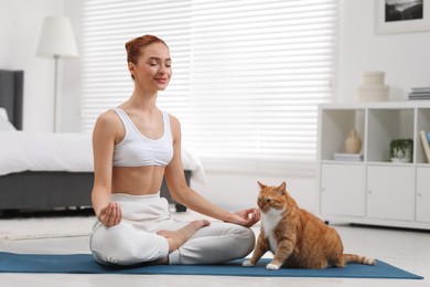 Beautiful woman with cute red cat practicing yoga on mat at home