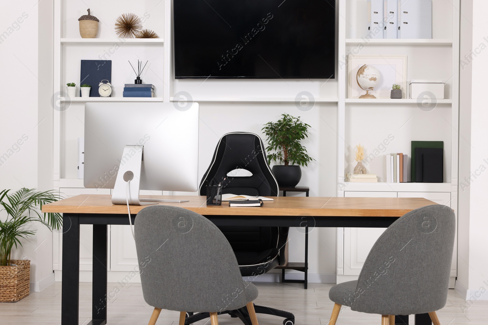 Photo of Stylish director's workplace with wooden table, tv zone, shelves and comfortable armchairs in room. Interior design