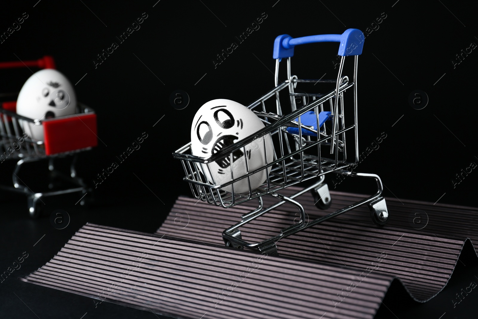 Photo of Egg with drawn scared face in shopping cart stunting on black background