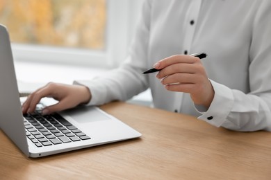 Photo of Woman with pen working on laptop at wooden table, closeup. Electronic document management