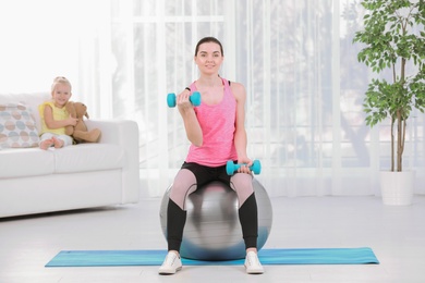 Woman doing fitness exercises while her daughter sitting on sofa at home