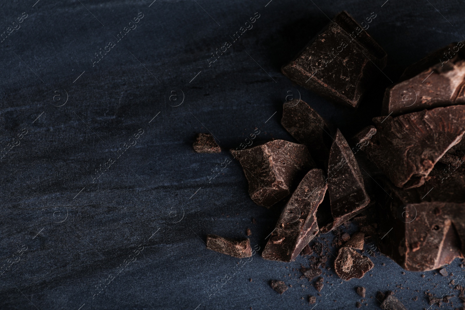 Photo of Pieces of dark chocolate on blue marble table, flat lay. Space for text