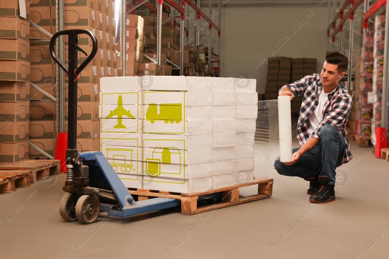 Image of Worker wrapping boxes with shipping icons in stretch film at warehouse