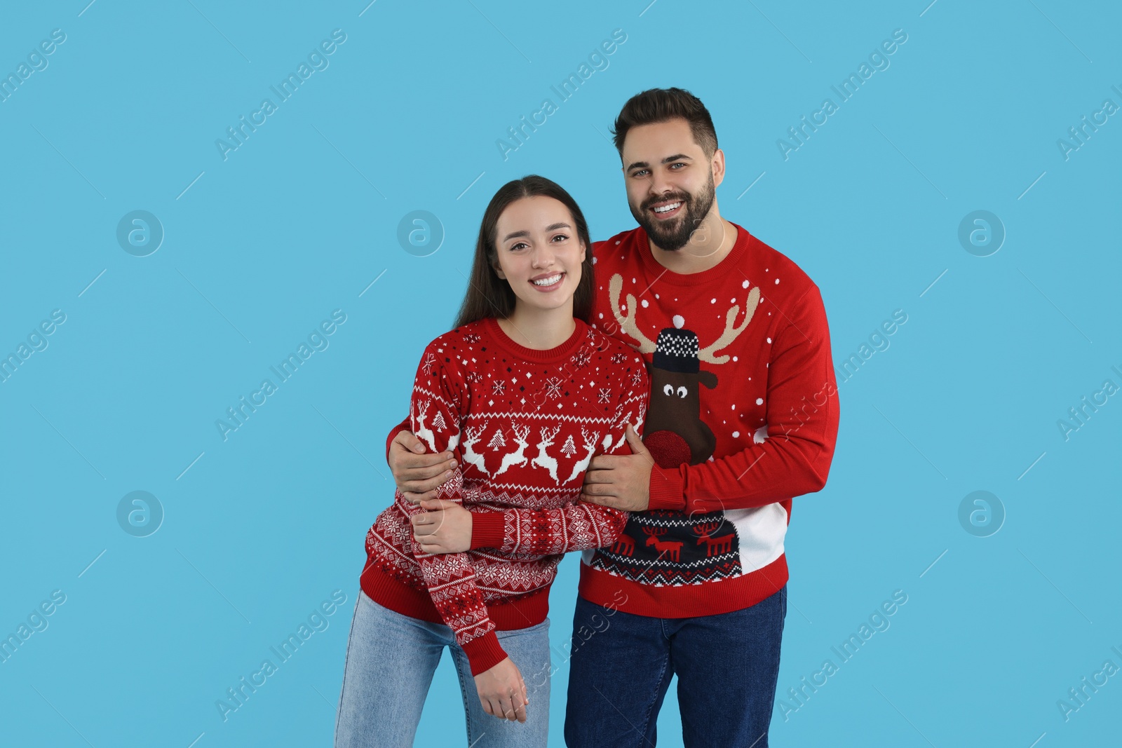 Photo of Happy young couple in Christmas sweaters on light blue background