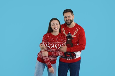Photo of Happy young couple in Christmas sweaters on light blue background