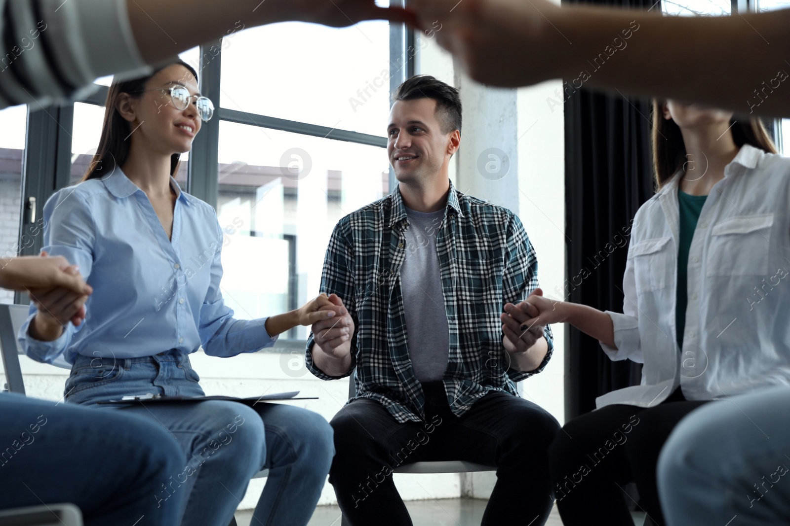 Photo of Psychotherapist holding hands with patients during group therapy session indoors