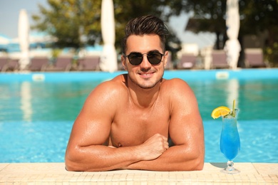 Photo of Young man with cocktail in pool on sunny day