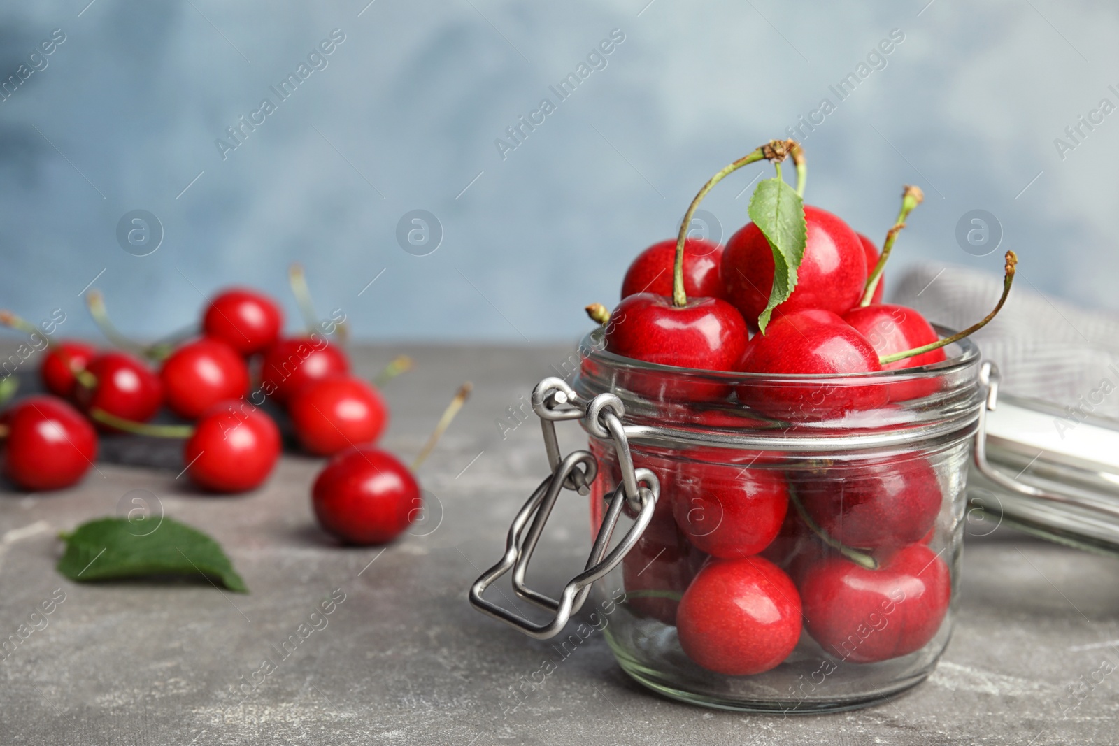 Photo of Glass jar with ripe sweet cherries on grey table. Space for text