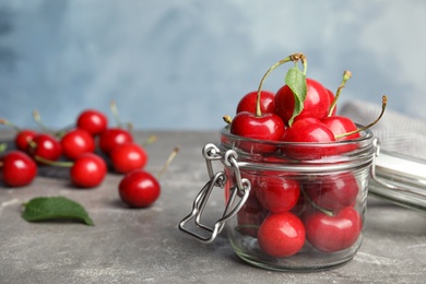 Glass jar with ripe sweet cherries on grey table. Space for text