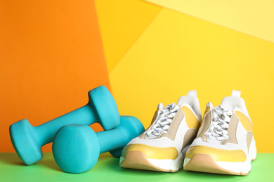 Photo of Dumbbells and modern sneakers on green table. Physical fitness