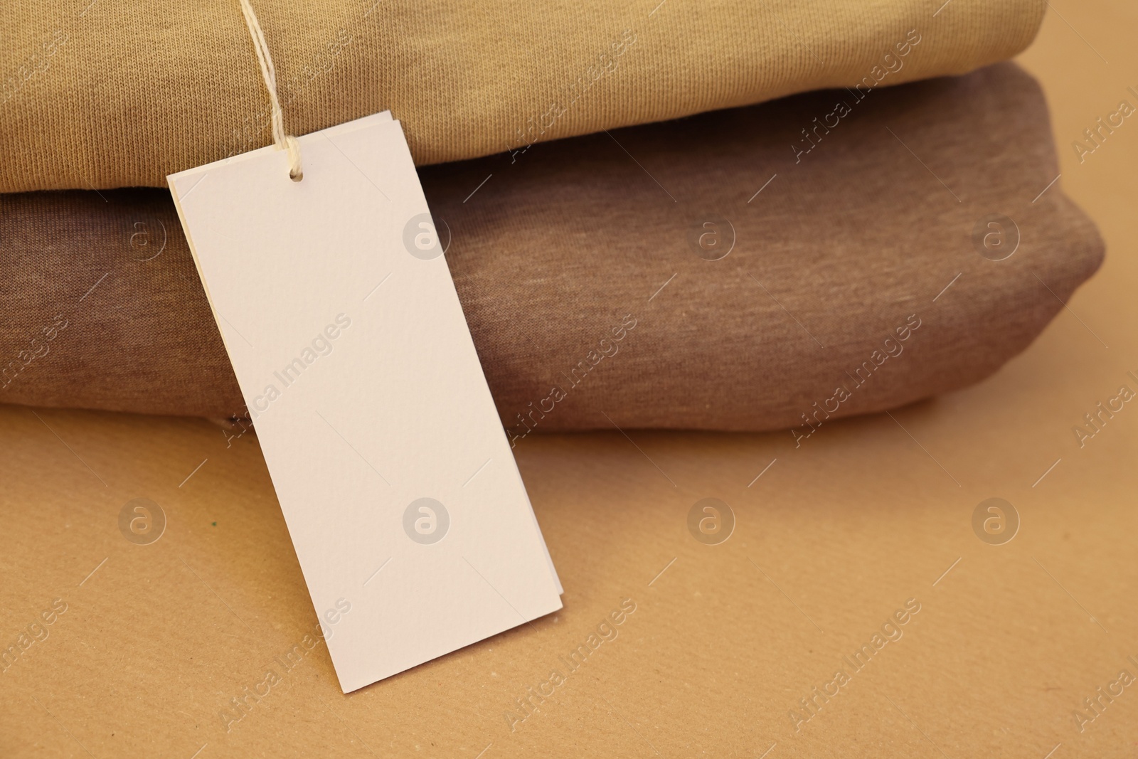 Photo of Garment with cardboard tag on kraft paper sheet, closeup. Space for text