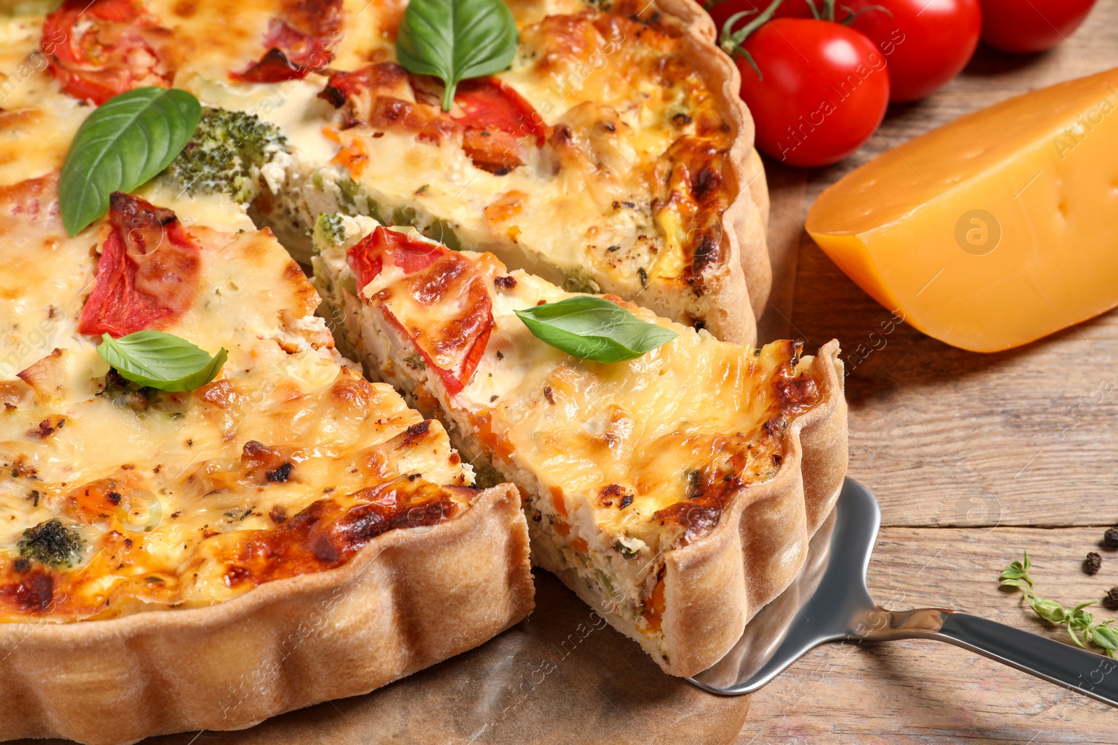 Photo of Taking piece of tasty quiche with tomatoes, basil and cheese on wooden table, closeup