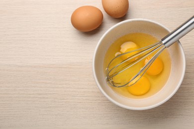 Photo of Whisk and eggs in bowl on wooden table, flat lay. Space for text