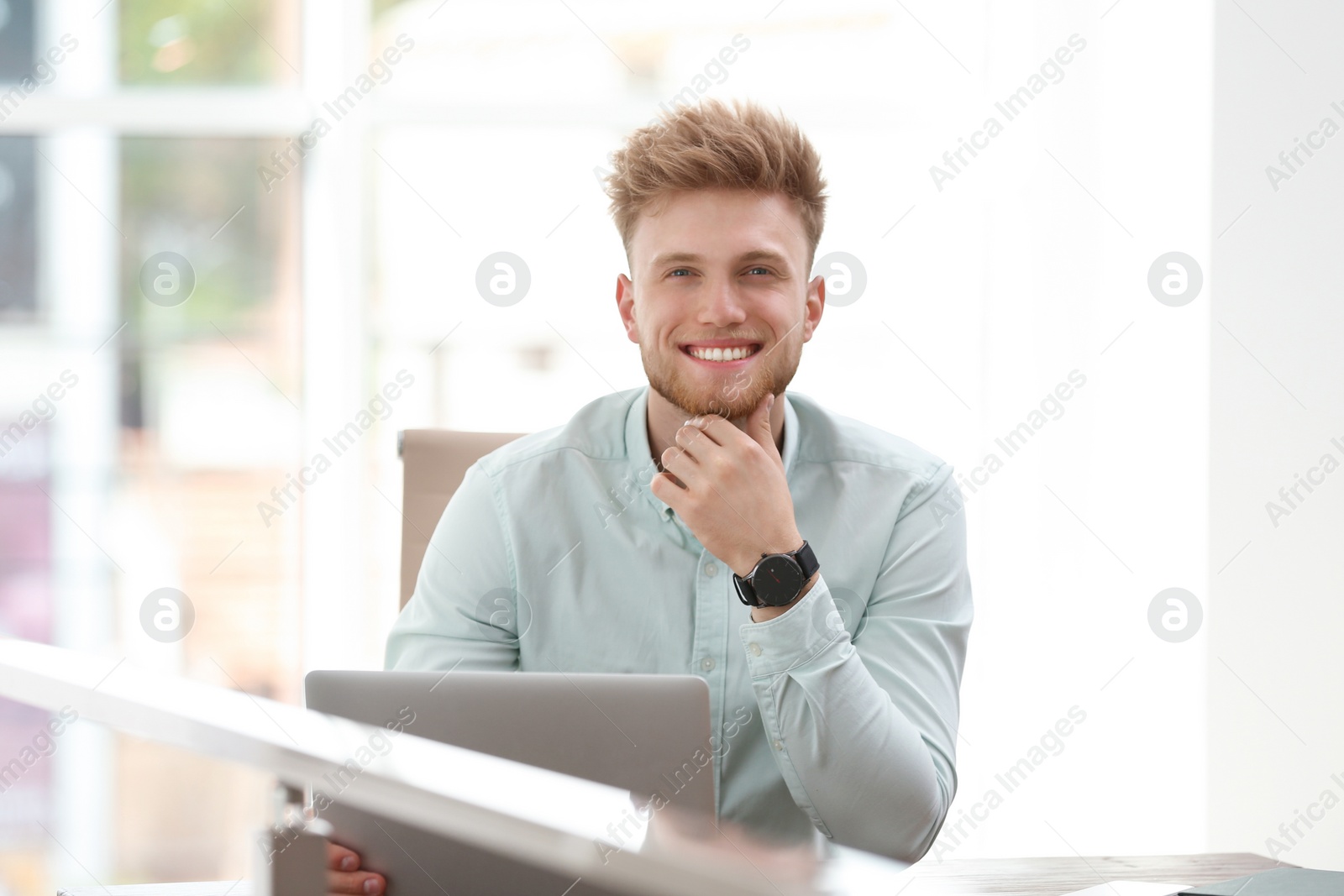 Photo of Portrait of handsome young man sitting at desk in office