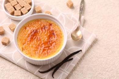 Delicious creme brulee in bowl, vanilla pods, sugar cubes and spoon on light textured table, closeup