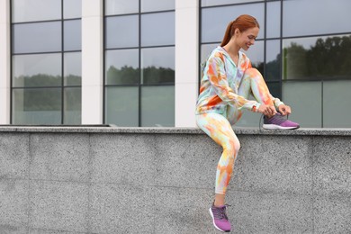 Photo of Woman sitting on parapet and tying shoelace of sneakers on street, space for text