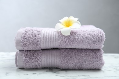 Photo of Violet terry towels and plumeria flower on white marble table, closeup