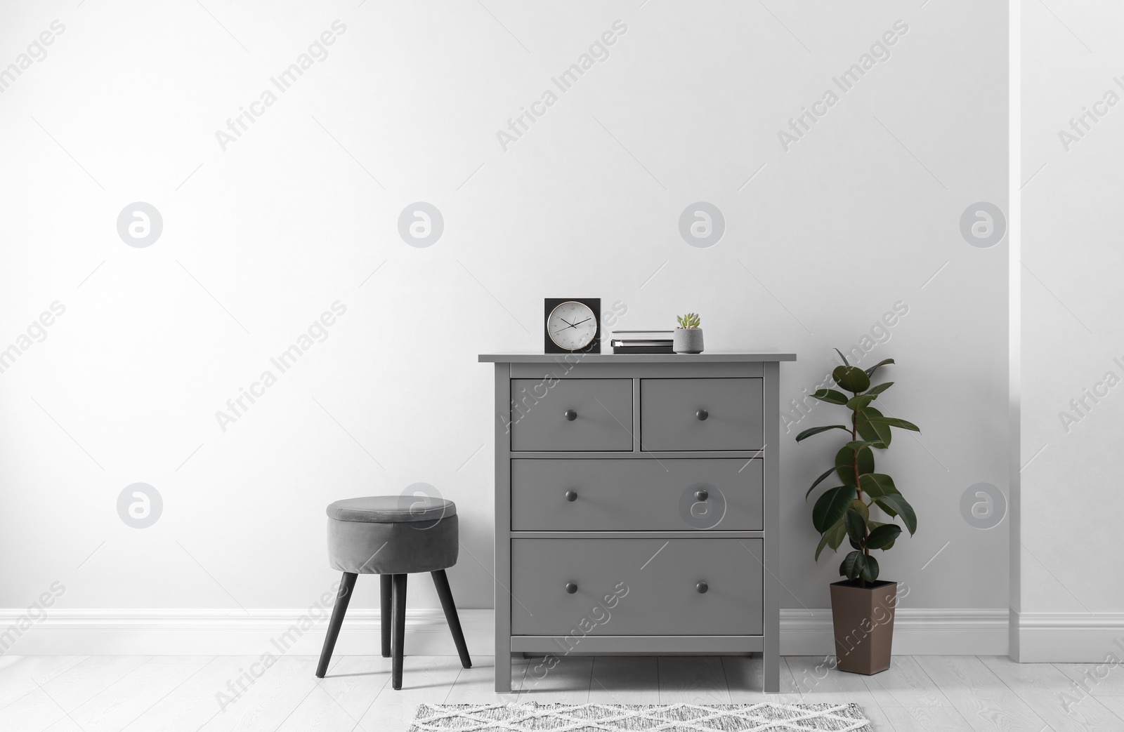 Photo of Elegant room interior with stylish chest of drawers, pouf and houseplant