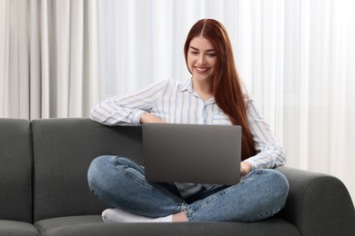 Photo of Happy woman using laptop on couch indoors