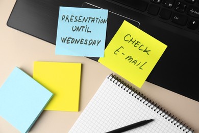 Photo of Laptop with reminder notes and notebook on beige desk, flat lay