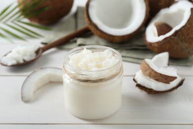 Photo of Jar of organic coconut cooking oil and fresh fruits on white wooden table, closeup