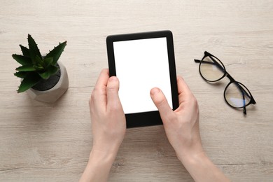 Photo of Woman using e-book reader at white wooden table, top view