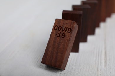 Photo of Falling wooden domino tiles on white table, closeup. Spreading of coronavirus concept