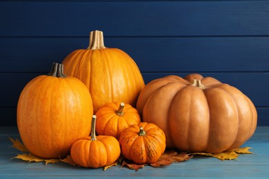 Photo of Pile of ripe pumpkins and dry leaves on turquoise wooden table