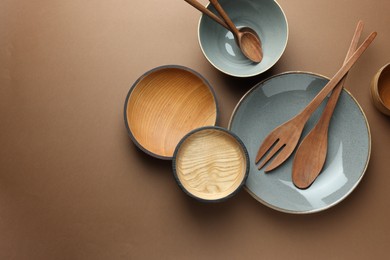Photo of Stylish empty dishware and wooden cutlery on brown background, flat lay. Space for text