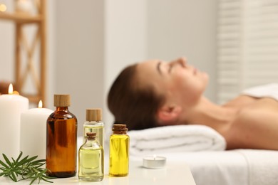 Photo of Aromatherapy. Woman relaxing on massage couch in spa salon, focus on bottles of essential oils, burning candles and rosemary