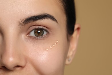 Photo of Young woman with gel on skin under eye against beige background, closeup