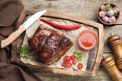 Photo of Piece of baked pork belly served with sauce and chili pepper on wooden table, flat lay