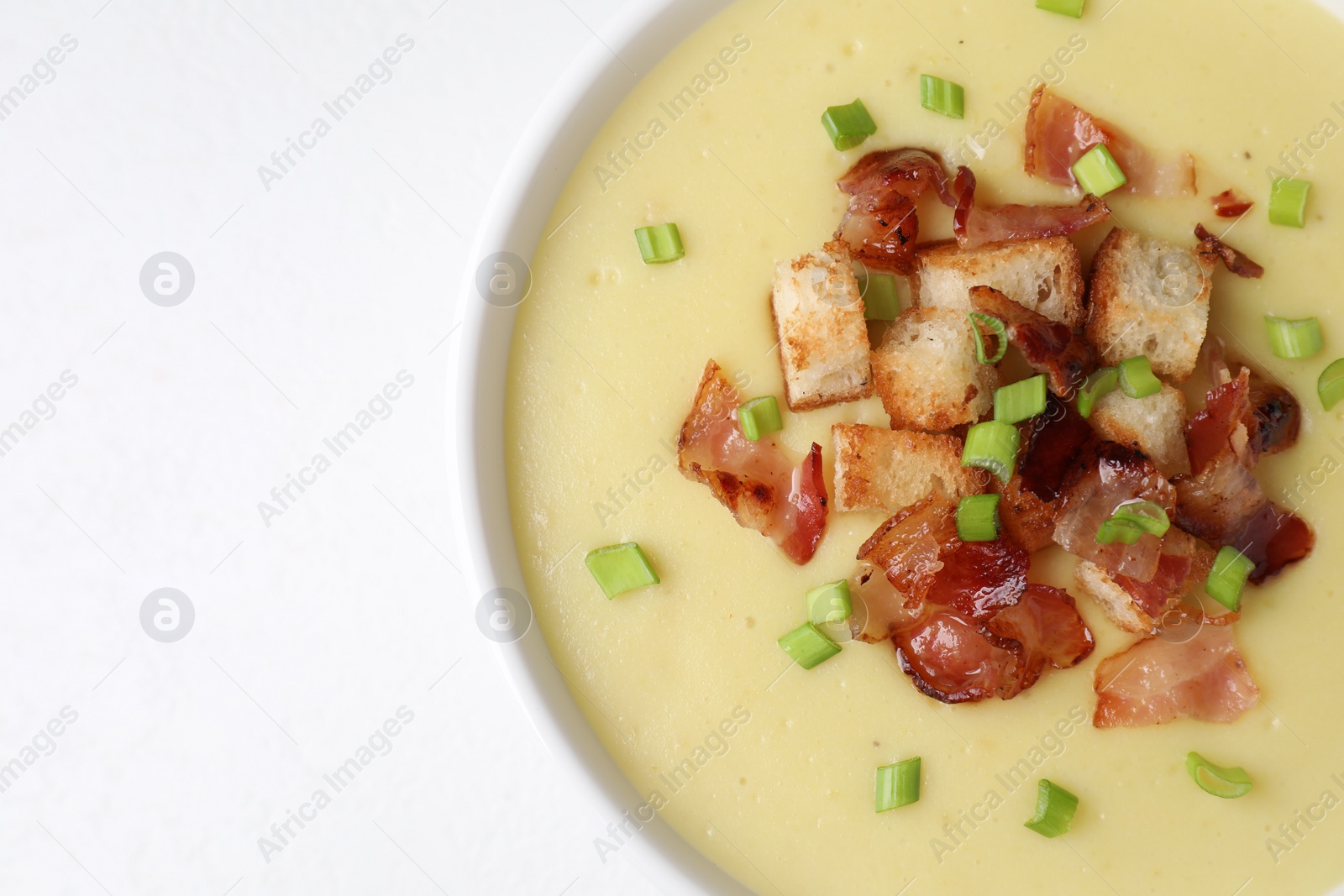 Photo of Tasty potato soup with bacon, green onion and croutons in bowl on white table, top view. Space for text