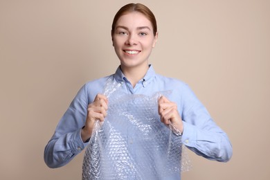 Photo of Woman popping bubble wrap on beige background. Stress relief